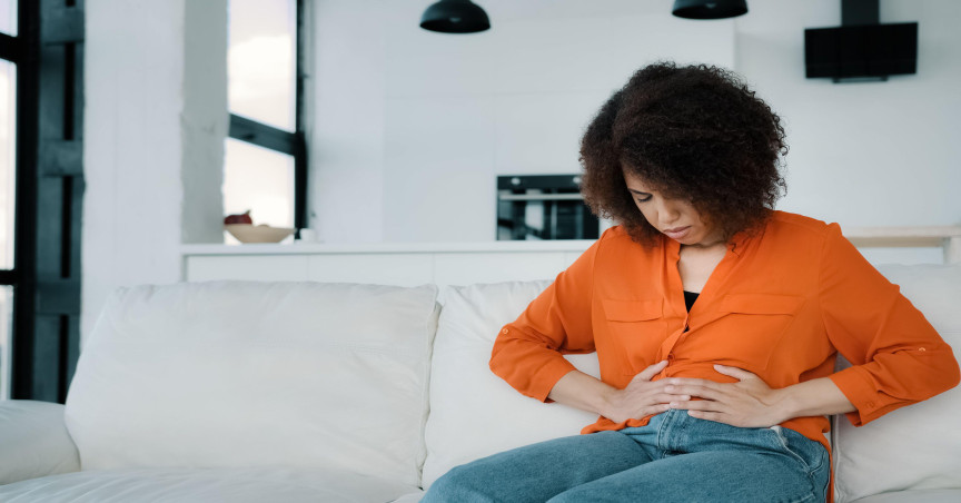 A woman sitting on the sofa at home, holding her stomach in discomfort